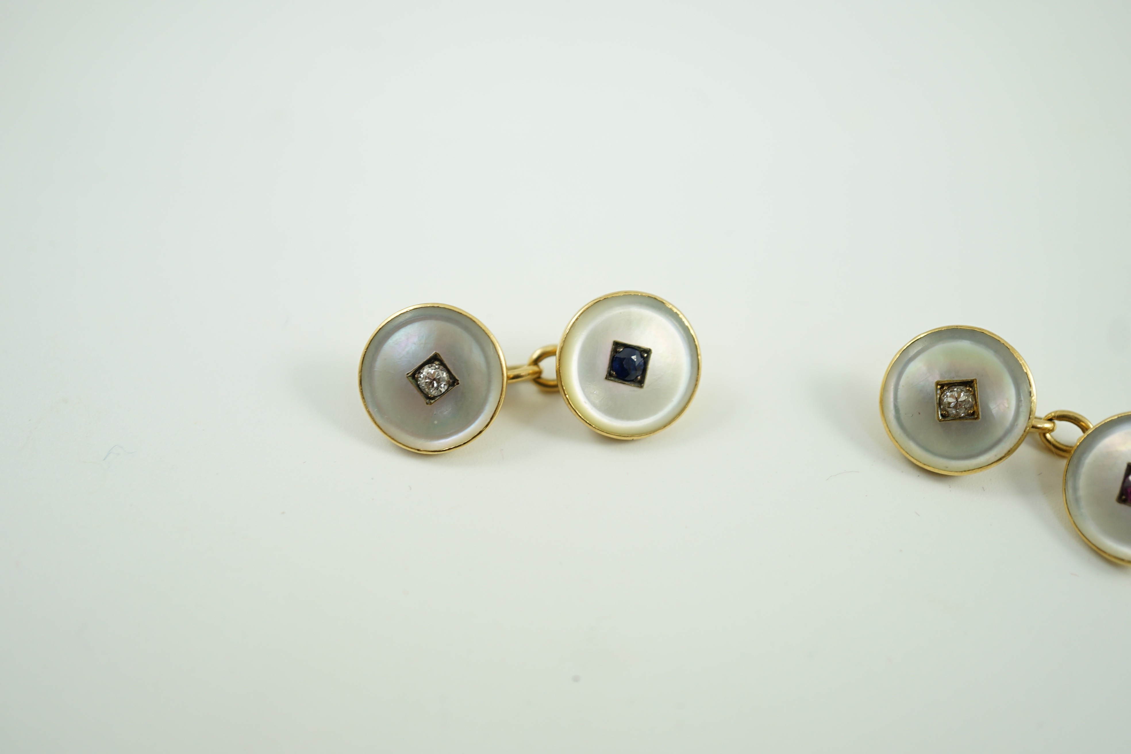 A pair of early to mid 20th century yellow metal mounted mother of pearl and gem set cufflinks, one set with a ruby and diamond, the other with a sapphire and diamond, link diameter 12mm, gross weight 8 grams.